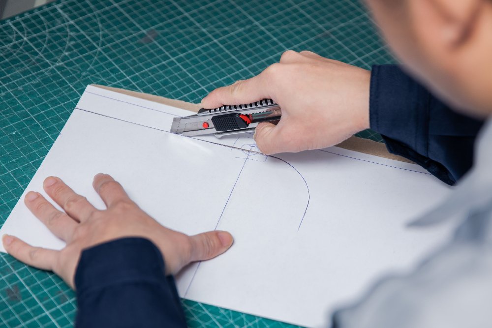 A worker is meticulously cutting out paper patterns.